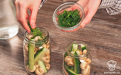 Уложите в банки овощи со специями. Подготовленные огурцы и шампиньоны плотно уложите в вымытые банки. Разложите в каждую равные части укропа и чеснока. Добавьте специи (лавровый лист и горошины переца). Уксус влейте в банки по одной десертной ложке на один литр емкости.