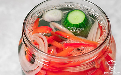 Заполните банку огурцами, помидорами, луком и сладким перцем. Залейте содержимое банки кипятком, оставьте на 10 минут под крышкой. Аккуратно слейте воду, она больше не понадобится.