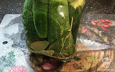 В банку положить огурцы, листья вишни и смородины, петрушку, перец горошком, гвоздику, зонтик укропа и зубчик чеснока. Залить в банку кипяток на 15-20 минут, после чего слить его и снова довести до кипения.