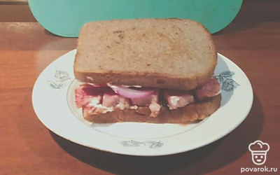 Сверху на грудинку положите лук и помидор. Закройте сэндвич второй половинкой хлеба. Блюдо готово.