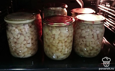 Готовую вареную фасоль переложить из кастрюли в подготовленные банки, накройте крышками и поставьте снова в духовку минут 15. После того как фасоль закипит, выключите духовку. Закрутите крышки. Готовые банки переверните вверх дном, накройте теплым одеялом, пледом (курткой) и оставьте так остывать до полного остывания естественным путем.