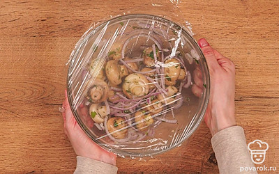 Подготовьте шампиньоны к маринованию. Когда из грибов испарится вся жидкость, влейте маринад в сковороду. Тушите под закрытой крышкой 10 минут на медленном огне. Затем переложите грибы в кастрюлю или миску, добавьте чеснок, лук и укроп, тщательно перемешайте. Закройте миску пищевой плёнкой. Грибы должны мариноваться после остывания 1,5-2 часа.