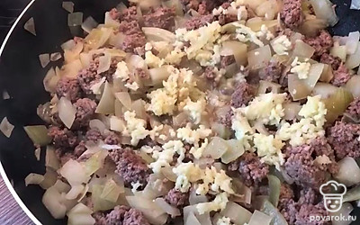 Добавить на сковороду фарш, нарезанный мелко лук, мелко нарезанный чеснок. Обжарить 10-12 минут, постоянно помешивая. Посолить и поперчить по вкусу.