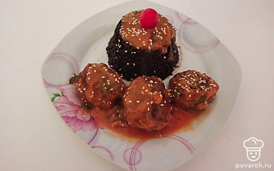 На тарелку выложите любой гарнир. Например, через формовочное кольцо выложите черный рис и хорошо его утрамбуйте. Рядом выложите несколько тефтелей и полейте их соусом. Сверху посыпьте кунжутом и украсьте свежими овощами.