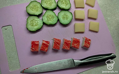 Нарежьте все составляющие на кусочки толщиной 0,5-1 сантиметр: огурцы — кружочками, сыр — квадратиками 2 на 2 сантиметра, крабовые палочки — кусочками по 2 сантиметра. 