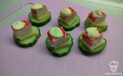 На кружочек огурца выложите сыр. Далее положите кусочек крабовый палочки. Сверху выдавите немного майонеза. 