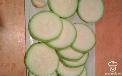 Кабачок вымойте, нарежьте колечками по 0.5 см, чеснок очистите.