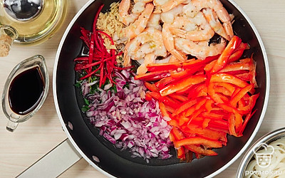 Приготовьте рамен с креветками. В глубокой сковороде в масле обжарьте репчатый и зеленый лук, перец чили и сладкий перец, имбирь, креветки 3-5 минут. Влейте соевый, устричный соус, кунжутное масло и 150 мл воды. Перемешайте. Дайте закипеть, добавьте лапшу, хорошо прогрейте.