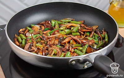 На разогретую сковороду добавьте нарезанные шампиньоны, лук, растительное масло, зеленую фасоль. Обжаривайте до золотистости.