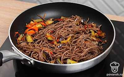 Выложите в сковороду отваренную собу и влейте соевый соус. Перемешайте и обжаривайте все ингредиенты вместе еще пару минут.