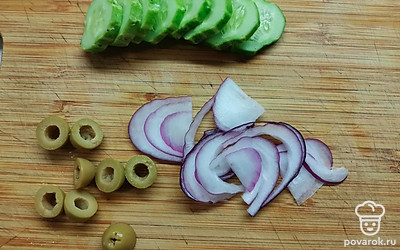 Огурец нарежьте кружочками толщиной 0,5 сантиметров, лук — полукольцами. Оливки разрежьте пополам. 