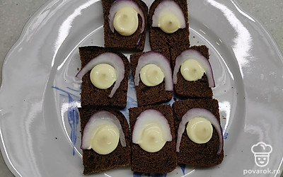 На каждый кусочек выдавите немного майонеза и выложите кусочек лука. 