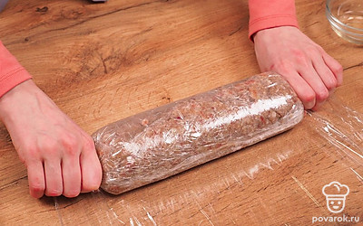 Сформируйте колбасу. На стол постелите пищевую пленку в два слоя. Выложите на нее фарш, придайте ему форму, плотно обернув пищевой пленкой. Концы пленки хорошо завяжите. Укрепите колбасу жгутиками из той же пленки, чтобы в ходе приготовления пленка не разошлась.