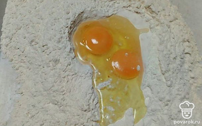 Просейте муку. Высыпьте ее на ровную поверхность, сделайте в муке воронку. Добавьте к муке сахар, ванилин и разрыхлитель. Вбейте 2 яйца.