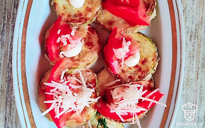 Обжаренные кабачки выложите на блюдо. На каждый кружок кабачка капните немного майонеза. Сверху положите дольку помидора, посыпьте чесноком и пармезаном.