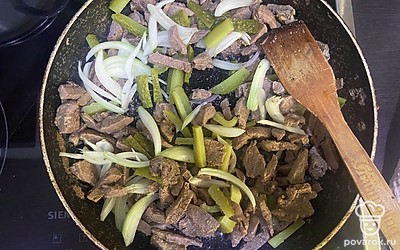 Выложите лук и огурец. Обжаривайте вместе с мясом минут 7.