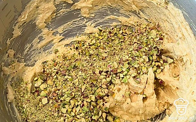 Высыпьте измельченные фисташки в массу. После перемешивания введите муку, щепотку соды и измельченный белый шоколад. Финально смешайте все ингредиенты до плотного, однородного теста.