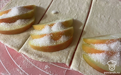 На половинку каждой части выложите дольки яблок, присыпанные сахаром. 