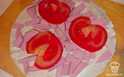Нарежьте колбасу полосками, помидор — кольцами. Выложите ингредиенты на лаваш.