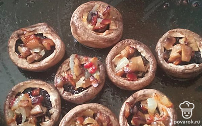 Шляпки выложите в сковороду с растительным маслом. Тушеный лук и ножки шампиньонов выложите в шляпки.