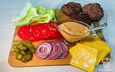 Нарежьте лук кольцами, помидор — на ломтики. Огурчики нашинкуйте потоньше. Выберете самые аппетитные листья салата айсберг. Приготовьте все ингредиенты к сборке.