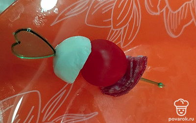  Тонкий кусочек любой сырокопченой колбасы сложите 2 раза. Насадите на шпажку.