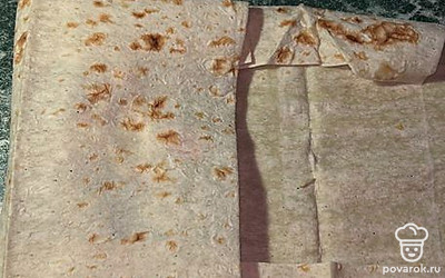 Сверните лаваш. Сначала подогните верх и низ лаваша, затем аккуратно скрутите. Конец немного смажьте соусом, чтобы склеить между собой. 