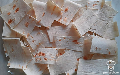 Форму для выпечки смажьте чесночным маслом и выложите в нее кусочки лаваша.