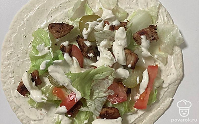 Выложить на лепешку мясо и овощи, равномерно смазав соусом. Оставить место по краям, чтобы во время обжарки ничего не вываливалось. Добавить соус к ингредиентам, так шаурма будет сочнее.
