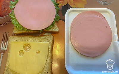 Затем на лист салат выложите колбасу. А на колбасу — растопленный сыр.