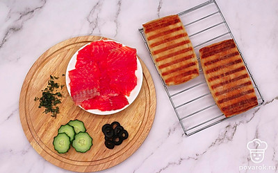 Слабосоленый лосось нарежьте кусочками. Огурец нашинкуйте тонко, маслины измельчите колечками. Укроп мелко порубите.