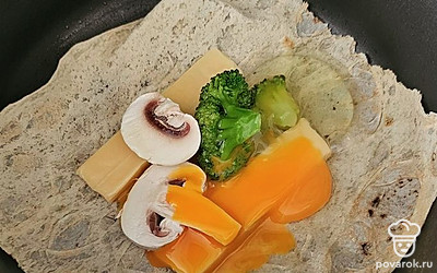 Затем выложите лаваш. На него положите сыр, грибы и овощи. Вбейте яйцо.