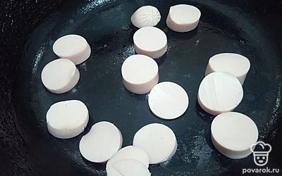 На сковороду выложите нарезанную колечками сосиску.