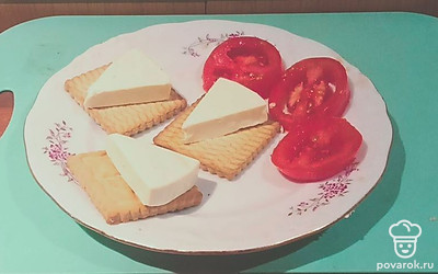 Нарежьте помидор поперек на круглые ломтики. Уложите кусочки плавленого сыра на печенье.