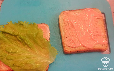 Ломтики хлеба смажьте сметаной и томатной пастой. Выложите листья салата.