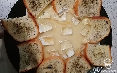 Сыр вместе с упаковкой, на которой он запекался, выложить в центр большого блюда. Вокруг разложите гренки. Подавайте закуску сразу после приготовления. Гренку окуните в расплавленный сыр и ешьте, запивая белым вином. 