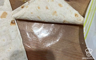 Смесь из колбасы с сыром выложите на край полоски из лаваша, сверните в треугольник-конверт.