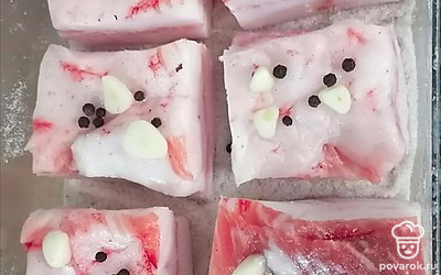 На дно контейнера насыпьте соль (слоем 1 сантиметр), выложите кусочки сала на расстоянии друг от друга (примерно 1 сантиметр). На каждый кусочек сала положите 2 кусочка чеснока и черный перец горошком. 