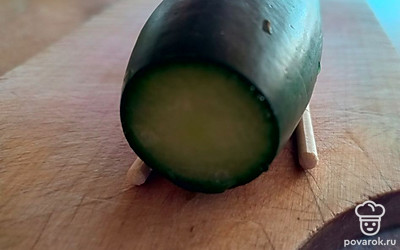 Помойте огурец и отрежьте кончики. Положите огурец на две палочки для удобства: нарезка будет необычной.