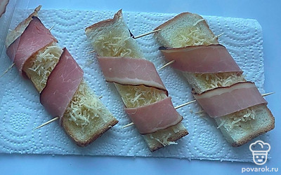 Оберните кусочки тоста окороком. Закрепите зубочистками или шпажками, чтобы при запекании мясные ломтики не развернулись.