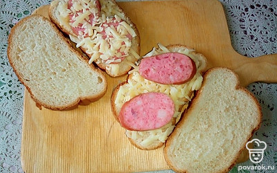 Нарежьте хлеб на кусочки и посыпьте одну половину всех нарезанных кусочков тертым сыром. Положите поверх сыра кусочки копченой колбасы и снова посыпьте сыром. Накройте кусочки хлеба с сыром и колбасой оставшейся половиной кусочков нарезанного хлеба.