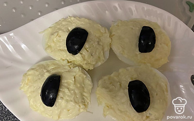 Выложите кусочки маслин на серединку яиц, имитируя зрачок.