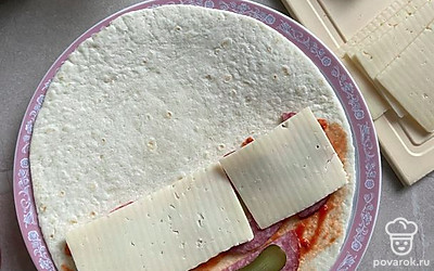 Смажьте половинку тортильи соусом и положите сверху колбаску, огурчики и сыр.