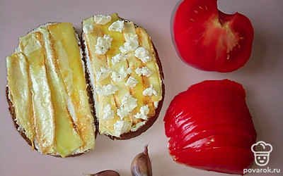 Добавьте небольшое количество творожного сыра в виде небольших капель на обжаренные полоски кабачка. Помидор нарежьте тонкими половинками кружков. Чеснок очистите и мелко нарежьте.