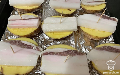 На противень, застеленный фольгой или пергаментом, выложите половинки картофеля. На каждый клубень положите ломоть сала и воткните в середину зубочистку. Запекайте картошку при 180 градусах 40-45 минут.