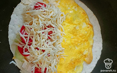 При помощи лопаточки переворачиваем тортилью с яйцом и выкладываем начинку на одну половину.