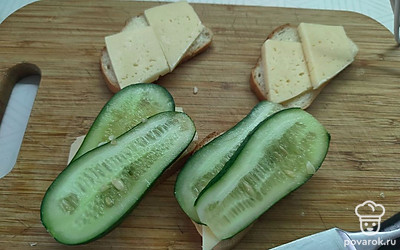 На два ломтика хлеба выложите тонко нарезанный огурец.