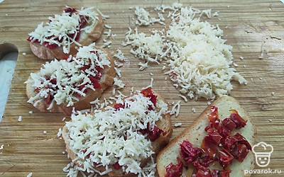 На батон положить вяленые томаты и чеснок. Сверху посыпать тертым сыром. 