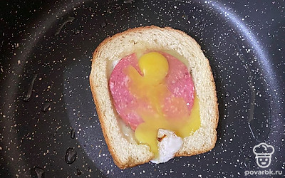 Положите в середину кусочки колбасы и разбейте яйца сверху. Пару минут бутерброд жарится открытым.