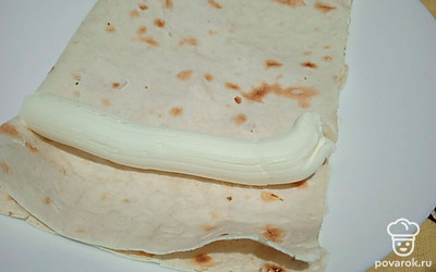 Половину лаваша сверните вдоль пополам, намажьте творожным сыром.